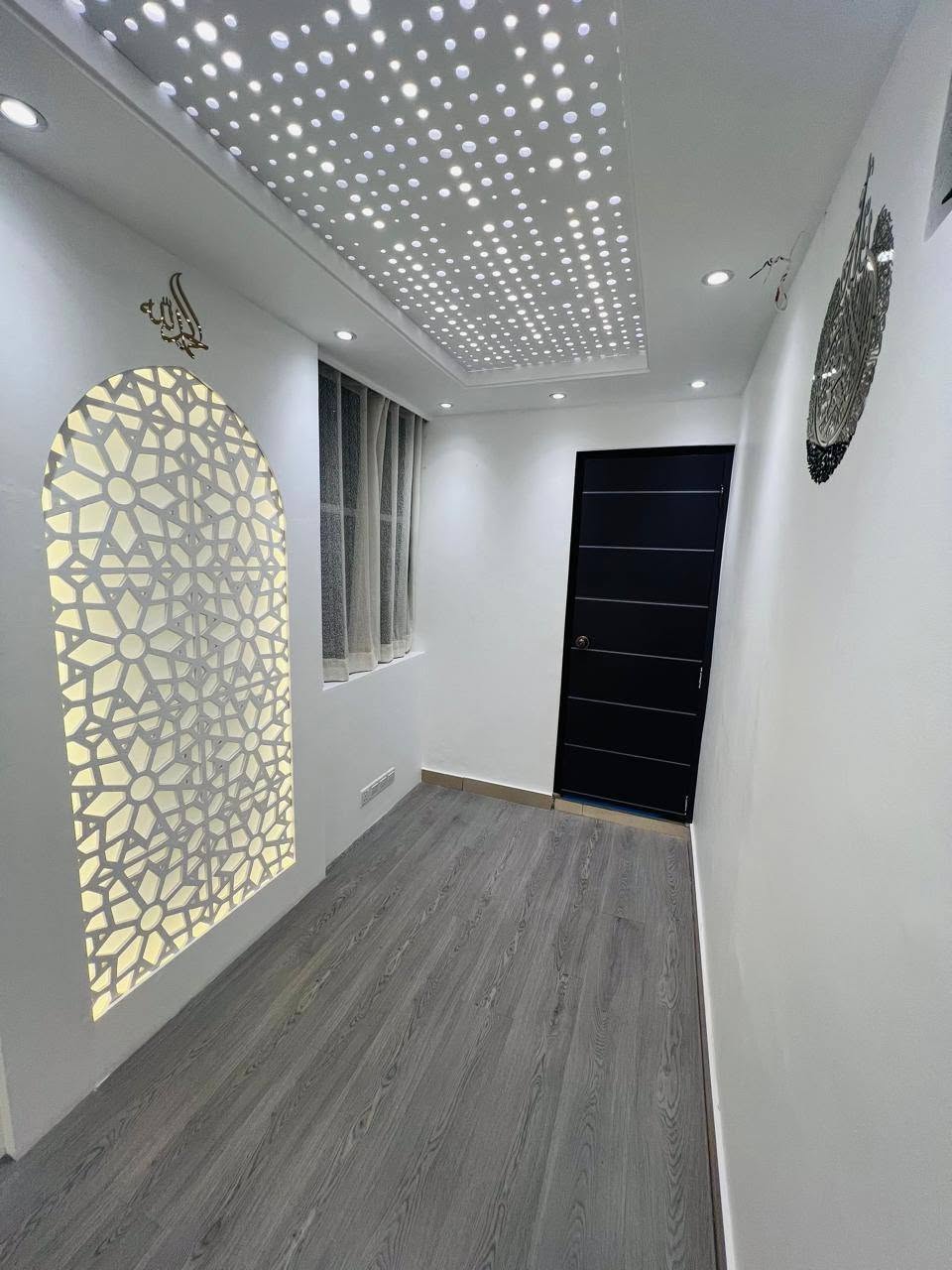 Prayer room with backlit geometric mihrab panel and perforated ceiling light