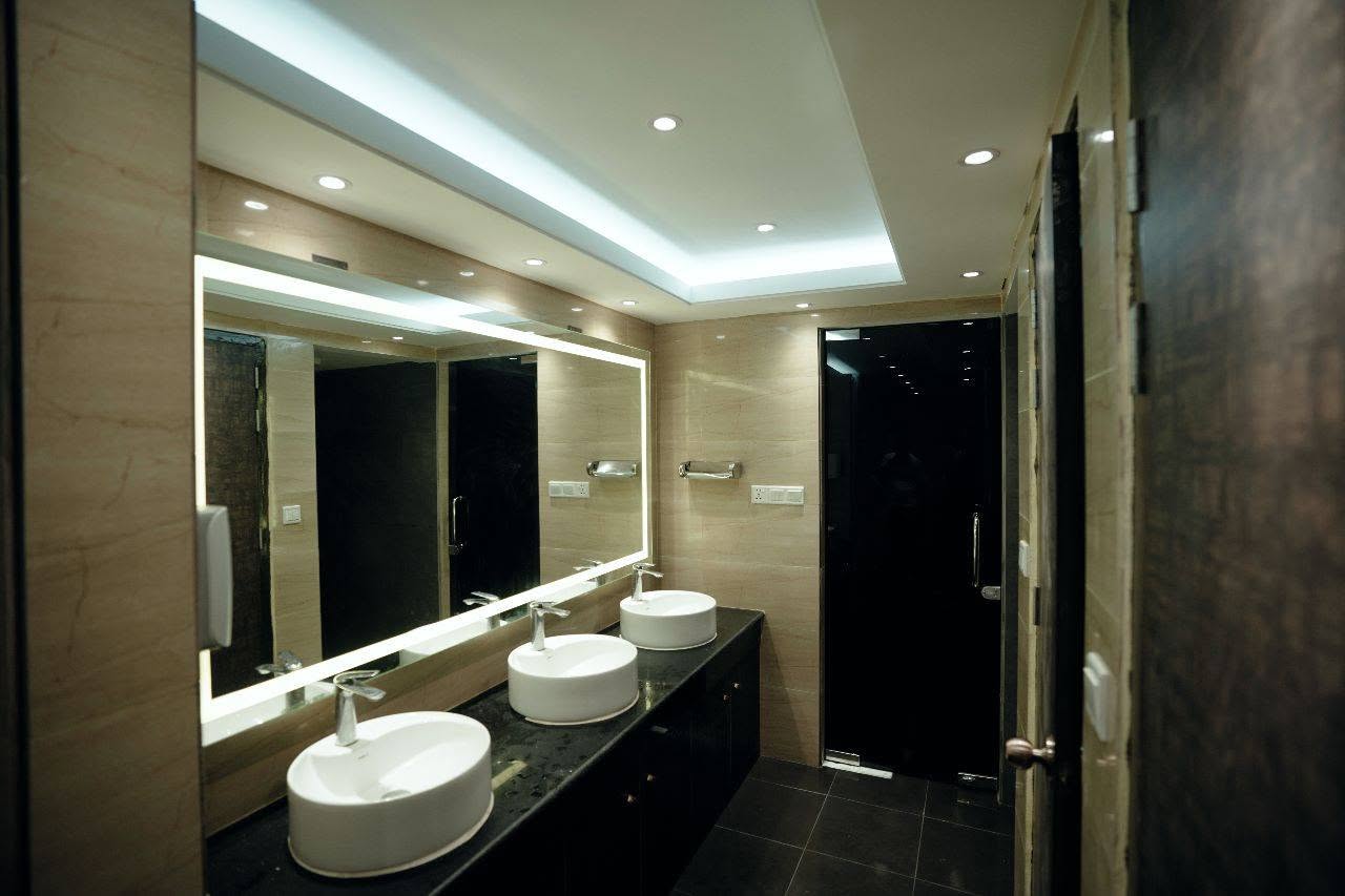 Marble washroom with backlit mirror, three basins and a shower cubicle